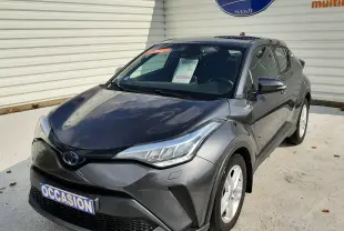 Toyota C-HR 1.8 Hybrid gris atlas métal vu en 3/4 avant droit, avec plaque "OCCASION" et logo Distinxion en arrière-plan.