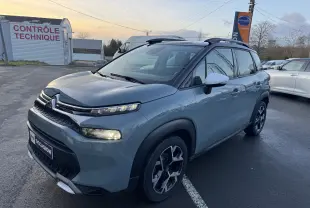 Vue 3/4 avant d'une Suzuki Swace hybride bleu foncé en showroom, avec calandre noire et jantes argentées.