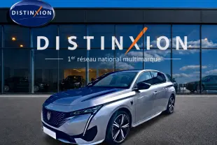 Peugeot 308 gris vue 3/4 avant droit, avec jantes alliage et phares LED distinctifs, devant showroom Distinxion.