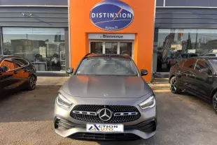 Vue de face d'une Mercedes GLA 200 d AMG Line gris montagne mat, calandre noire à étoiles chromées, stationnée devant un concessionnaire.