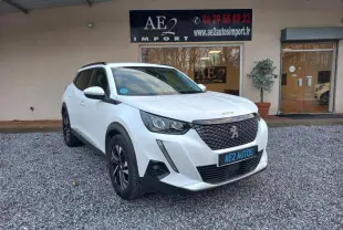 Peugeot 2008 blanc vue 3/4 avant droit, avec calandre noire et jantes alliage, stationné devant un bâtiment.