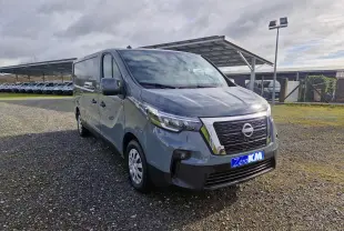 Nissan Primastar gris urbain en 3/4 avant droit, avec calandre chromée et plaque "Zero KM" visible.