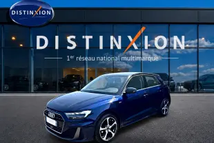 Audi A1 Sportback bleu foncé avec toit noir, vue 3/4 avant droit devant une vitrine Distinxion.