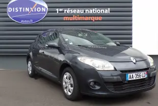 Renault Mégane III berline anthracite bleuté vue 3/4 avant droit avec phares allumés devant un mur gris.