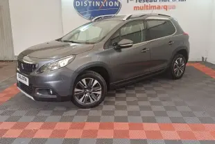 Peugeot 2008 gris foncé en 3/4 avant droit, avec jantes alliage et barres de toit chromées visibles.