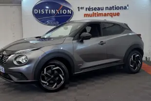 Nissan Juke Hybrid gris foncé vu de profil droit en intérieur, avec jantes noires et détails hybrides visibles.
