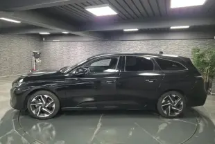 Peugeot 308 SW noire vue de profil côté gauche, jantes alliage 17'' et vitres surteintées en intérieur showroom.