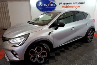 Renault Captur Intens E-Tech hybride rechargeable gris clair, vue 3/4 avant droit avec jantes distinctives et feux LED allumés.