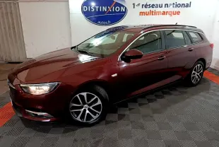 Opel Insignia break rouge vue 3/4 avant droit avec jantes alliage et phares allumés en intérieur showroom.