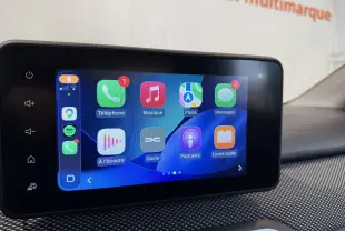 Vue 3/4 avant droite d'une Dacia Sandero grise en showroom avec plaque "OCCASION" visible sur le pare-chocs.