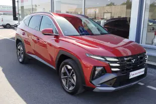 Hyundai Tucson 2024 hybride en Ultimate Red Métal, vu en 3/4 avant droit avec calandre noire et jantes bi-ton.