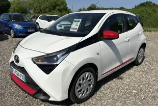 Toyota Aygo MC blanc vue 3/4 avant droit avec rétroviseurs rouges et bande rouge sur bas de caisse, en extérieur.