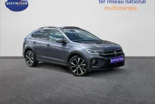 Volkswagen Taigo gris Ascot en 3/4 avant droit, avec jantes alu et barres de toit visibles.
