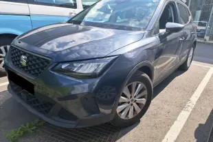 SEAT Arona gris magnétique en 3/4 avant droit, avec jantes alliage 16 pouces et barres de toit noires visibles.