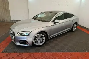 Audi A5 gris clair vue 3/4 avant droit dans un garage avec sol noir et rouge, jantes alliage multibranches.