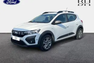 Vue 3/4 avant droite d'une Dacia Sandero Stepway blanche avec barres de toit et protections noires sur les bas de caisse.