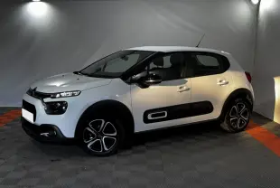 Citroën C3 blanche vue de profil droit en intérieur, avec protections latérales noires et jantes stylisées.