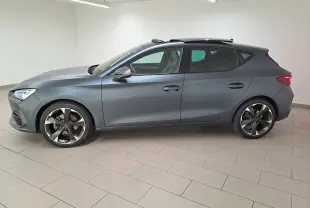 Vue de profil côté gauche d'une CUPRA Leon 2024 gris magnétique mat avec toit ouvrant panoramique en intérieur showroom.