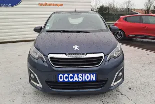 Peugeot 108 bleu vue 3/4 avant droit, avec jantes bi-ton et feux LED allumés sur parking extérieur humide.