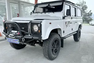 Land Rover Defender blanc vu 3/4 avant droit avec pare-buffle noir et pneus tout-terrain marqués BFGoodrich.