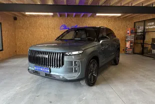 SUV JAECOO J7 gris olive en 3/4 avant droit, avec calandre verticale noire et toit noir dans un garage.