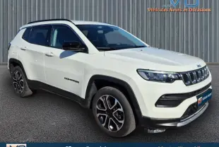 Jeep Compass blanc vue 3/4 avant droit, avec jantes 18 pouces et barres de toit noires sur fond urbain.