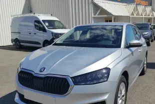 Vue 3/4 avant droite d'une Skoda Fabia 2023 gris alu avec calandre noire et phares LED, stationnée devant un bâtiment commercial.