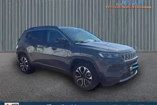 Jeep Compass gris en 3/4 avant droit, avec jantes 18 pouces et barres de toit visibles sur fond urbain.
