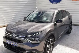 Citroën C4 gris 3/4 avant droit, avec phares LED et jantes alliage bicolores, stationné devant un mur blanc.