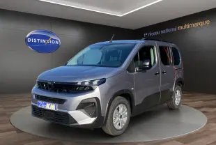 Peugeot Rifter gris clair vu en 3/4 avant droit, avec calandre noire et jantes argentées, en showroom intérieur.