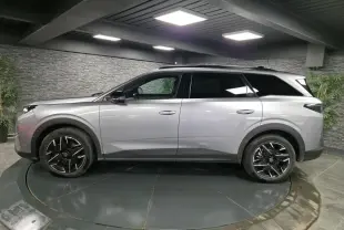 Vue de profil côté gauche d’un Peugeot 5008 gris métallisé avec jantes alliage noires dans un showroom.