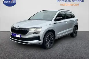 Vue 3/4 avant droite d'un Skoda Karoq argent 2025 avec barres de toit et jantes noires distinctives.