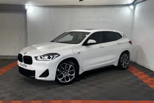BMW X2 xDrive25e blanc en 3/4 avant droit, avec jantes alliage et toit ouvrant panoramique visible.