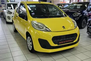 Vue 3/4 avant d'une Peugeot 107 jaune vif en showroom, avec calandre noire et logo lion visible sur le capot.