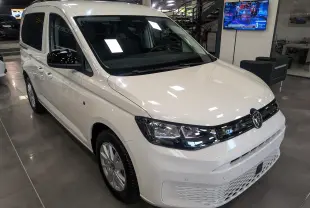 Vue 3/4 avant d'un Volkswagen Caddy blanc 2025 en showroom, avec calandre noire et jantes argentées.