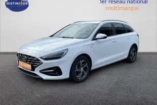Vue 3/4 avant droite d'une Hyundai i30 SW 2022 en blanc Atlas avec jantes alliage et calandre noire distinctive.