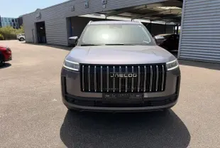 Vue 3/4 avant du JAECOO J5 gris Phantom avec calandre verticale noire et phares LED fins, stationné devant un bâtiment.