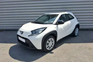 Toyota Aygo X blanc pur vue 3/4 avant droit, avec protections noires autour des roues et rétroviseurs noirs.