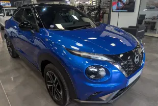 Vue 3/4 avant droit du Nissan Juke Hybrid 2025 en bleu magnétique avec toit noir et jantes noires en concession.