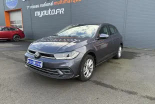 Volkswagen Polo gris cendre vue 3/4 avant droit, stationnée devant un mur gris avec logo Distinxion.