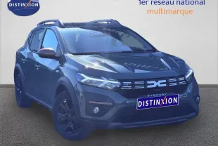 Vue 3/4 avant droite d'une Dacia Sandero Stepway 2025 en kaki lichen avec jantes noires et barres de toit.