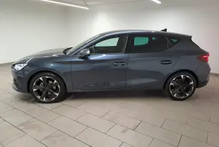 Vue latérale droite d'une CUPRA Leon 2023 gris magnétique avec jantes noires et feux arrière allumés dans un intérieur neutre.