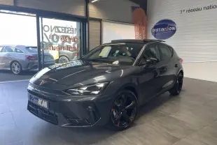 Vue 3/4 avant d'une CUPRA Leon gris magnétique avec jantes cuivrées et signature lumineuse Tri-LED en showroom.
