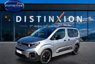 Citroën Berlingo Steel Grey vue 3/4 avant droit, avec jantes noires et barres de toit visibles devant vitrine Distinxion.