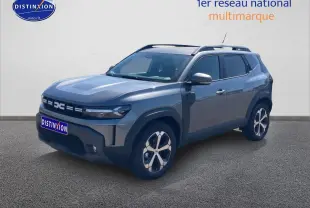 Dacia Duster gris schiste en 3/4 avant droit, avec jantes alliage et barres de toit visibles.