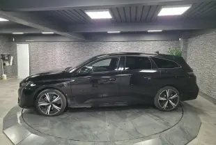 Peugeot 308 SW GT noire vue de profil côté gauche, jantes alliage 18'' et toit noir brillant en intérieur showroom.