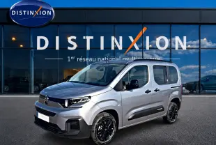 Citroën Berlingo Steel Grey en 3/4 avant droit, avec jantes noires et barres de toit visibles devant un bâtiment Distinxion.