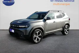 Dacia Duster gris schiste métal en 3/4 avant droit, avec jantes alliage bicolores et barres de toit visibles.