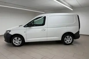 Vue de profil côté gauche d'un Volkswagen Caddy blanc Candy avec pare-chocs et protections noires, en intérieur.