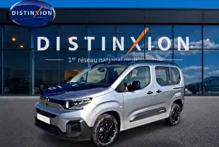 Vue 3/4 avant droit d'un Citroën Berlingo gris acier avec jantes noires devant une vitrine Distinxion.